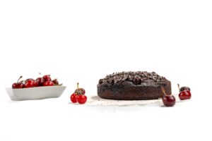 Zoom sulla torta al cacao vegana con ciliegie, riccioli di cioccolato e spolverata di cacao amaro, senza burro e senza uova