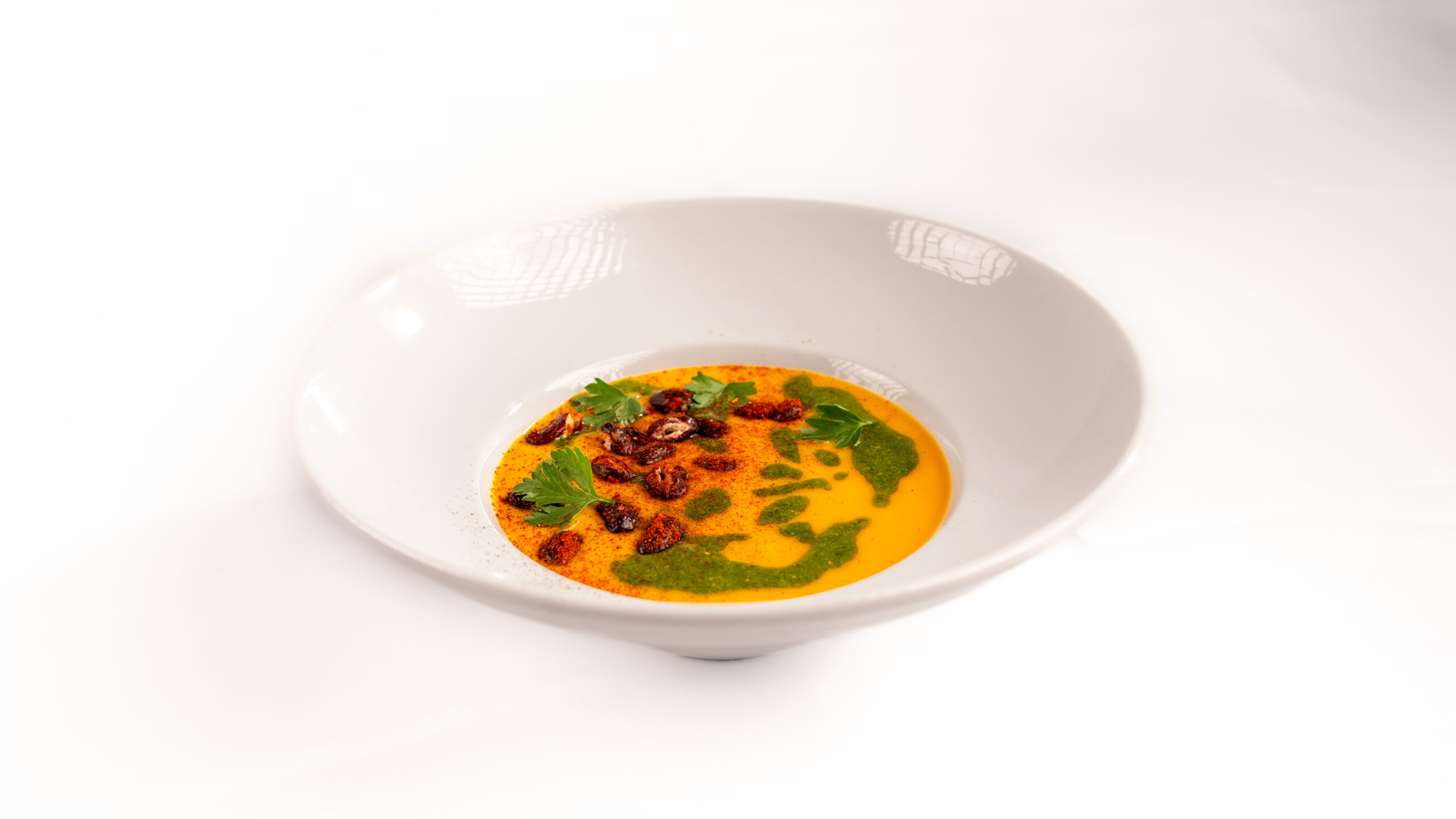 Vellutata di carote plant-based, piatto caldo invernale con pesto di barbe e fagioli croccanti.